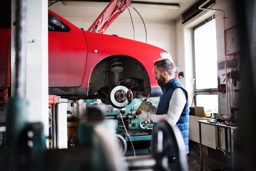 Nahaufnahme der freigelegten Bremsscheibe eines aufgebockten Fahrzeugs, dahinter der Mechaniker mit dem Werkzeug.