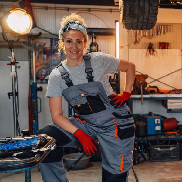 Porträt von Katrin Ostermann, Kfz-Meisterin und Inhaberin, mit Arbeitshandschuhen in der Werkstatt.