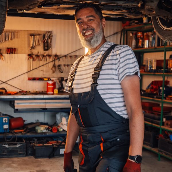 Porträt von Stefan Reiter, Kfz-Meister, im Latzhosen-Arbeitsanzug in der Werkstatt.